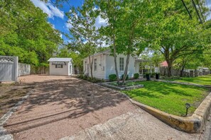 A residential property with a gravel driveway, a small white house, and a well-maintained lawn. - Romantic-Steps To Main-FirePit! (Fredericksburg)