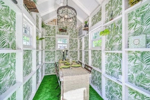 A room with a green artificial grass floor, white walls with a leaf pattern, a dining table set with green tablecloth and plates, and a hanging light fixture.