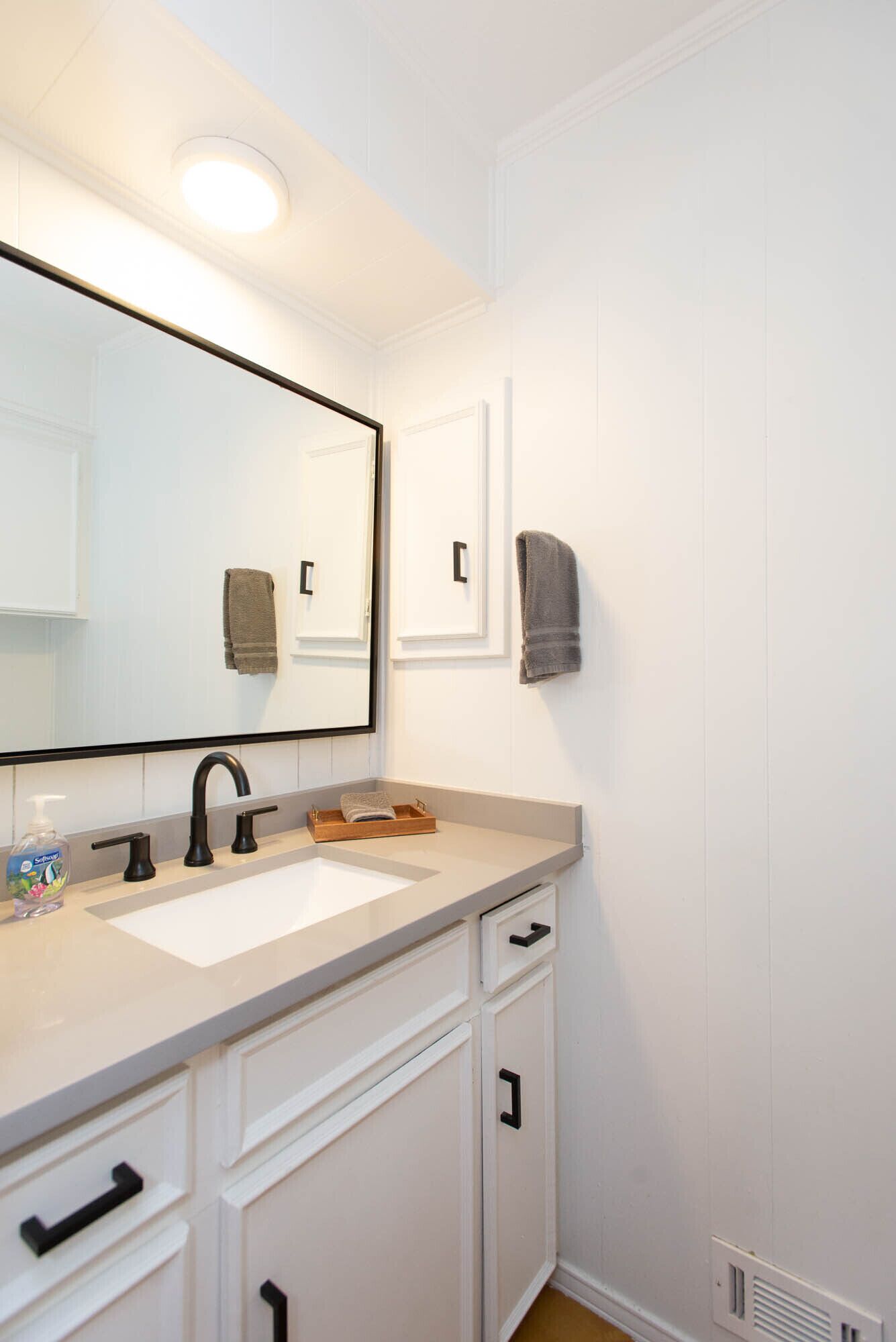 A bathroom with a white vanity, two sinks, a mirror, and a towel rack.
