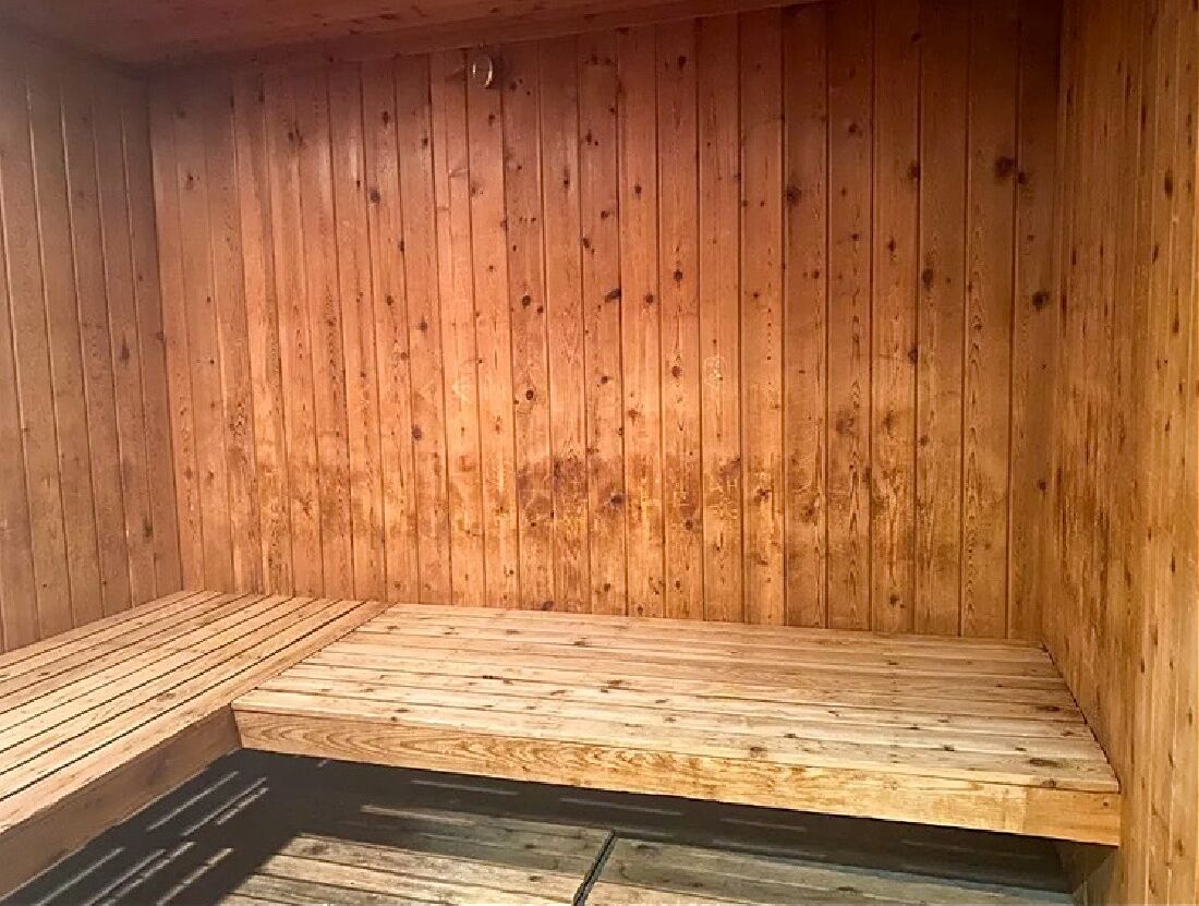 Una sauna de madera con un banco y un escalón pequeño que da acceso al agua.