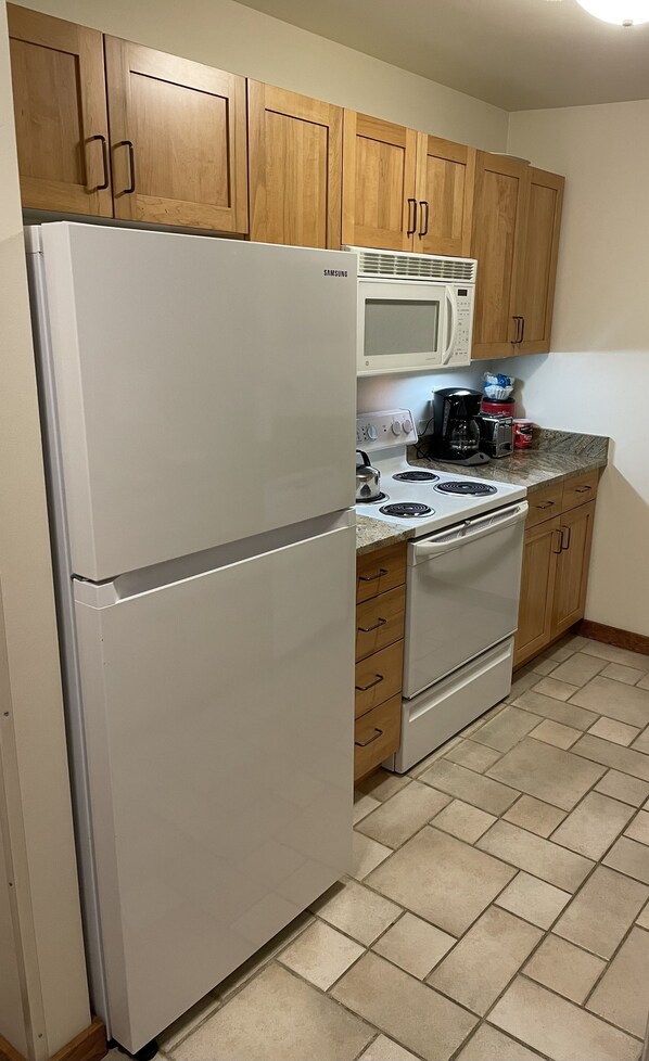 A kitchen with wooden cabinets, a white refrigerator, a microwave, a stove, and a coffee maker. - Kintla Condo Right on chair lift 3! (Whitefish)