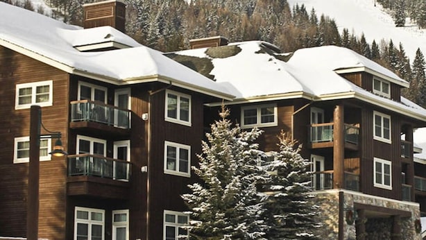 Un immeuble en bois à plusieurs étages, doté de balcons, entouré d’arbres couverts de neige et avec une chaîne de montagnes en arrière-plan.