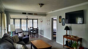 A living room with a sofa, coffee table, TV, and a dining area with a table and chairs. - Cozy Blue Cottage With Access To All Sports Lake.  (Greenville)