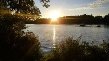 A serene lakeside view with trees framing the scene and the sun setting on the horizon.