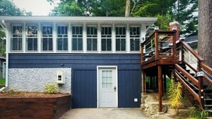 A two-story house with a blue exterior, a white door, and a wooden staircase leading to a deck. - Cozy Blue Cottage With Access To All Sports Lake.  (Greenville)