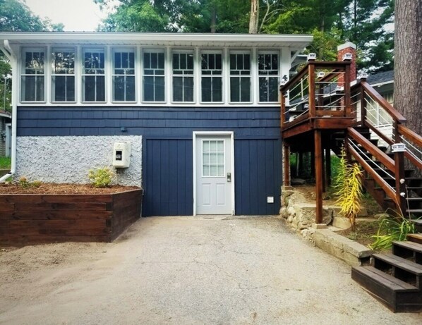 A two-story house with a blue exterior, a white door, and a wooden staircase leading to a deck. - Cozy Blue Cottage With Access To All Sports Lake.  (Greenville)