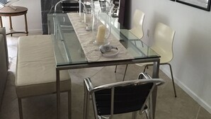 Un comedor moderno con una mesa de vidrio, sillas blancas y un camino de mesa de mármol. Hay obras de arte enmarcadas en las paredes y un espejo redondo sobre la mesa.