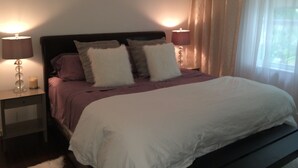 Un dormitorio con una cama, dos lámparas de noche y un ventanal con cortinas.