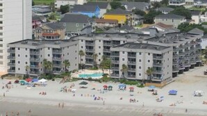 A beachfront hotel with multiple floors, a sandy beach, and several umbrellas. - Great Location, Family Friendly.  Beach Front 3Bedroom 3Bath Sleeps 10 (Murrells Inlet)