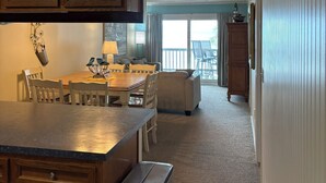 A kitchen with wooden cabinets, a dining table, and chairs. There is a trash can and a window with a view of the outside. - Great Location, Family Friendly.  Beach Front 3Bedroom 3Bath Sleeps 10 (Murrells Inlet)