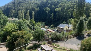 Une table de pique-nique est installée dans une zone herbeuse, offrant une vue sur une colline boisée et un bâtiment sur lequel on peut lire l’inscription « St. John’s Water ».