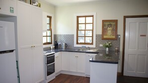 Une cuisine avec des meubles blancs, un four encastré, un évier et une fenêtre.