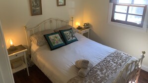 Un lit bien fait, avec une couvre-lit à motifs floraux et deux oreillers, une table de chevet avec une lampe, et une fenêtre donnant sur un beau paysage.