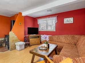 A living room with a red wall, a wooden staircase, a television, a sofa, and a small table with decorative items. - Penzion Jindřiška by Interhome (Tatobity)