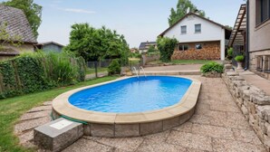 Un patio trasero residencial con piscina, escalones de piedra y una casa con muro de piedra y antena parabólica.
