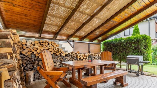 Un patio al aire libre con una mesa y sillas de madera, una parrilla y una pila de leña.