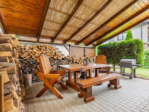 An outdoor patio with a wooden table and chairs, a grill, and a stack of firewood. - Penzion Jindřiška by Interhome (Tatobity)