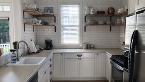 A modern kitchen with white cabinetry, wooden shelves, a stainless steel refrigerator, and a built-in dishwasher. - Vintage-inspired cottage in Seabrook, sleeps 7 (Pacific Beach)