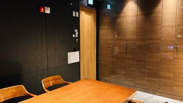 Un salón de conferencias con una mesa y sillas de madera, una pared negra con detector de incendios y un armario de madera con espejo.