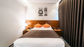 Camera d'hotel con un letto grande, una testiera in legno, due comodini con lampade e un tavolino da notte, e vista sulla Torre Eiffel dalla finestra.