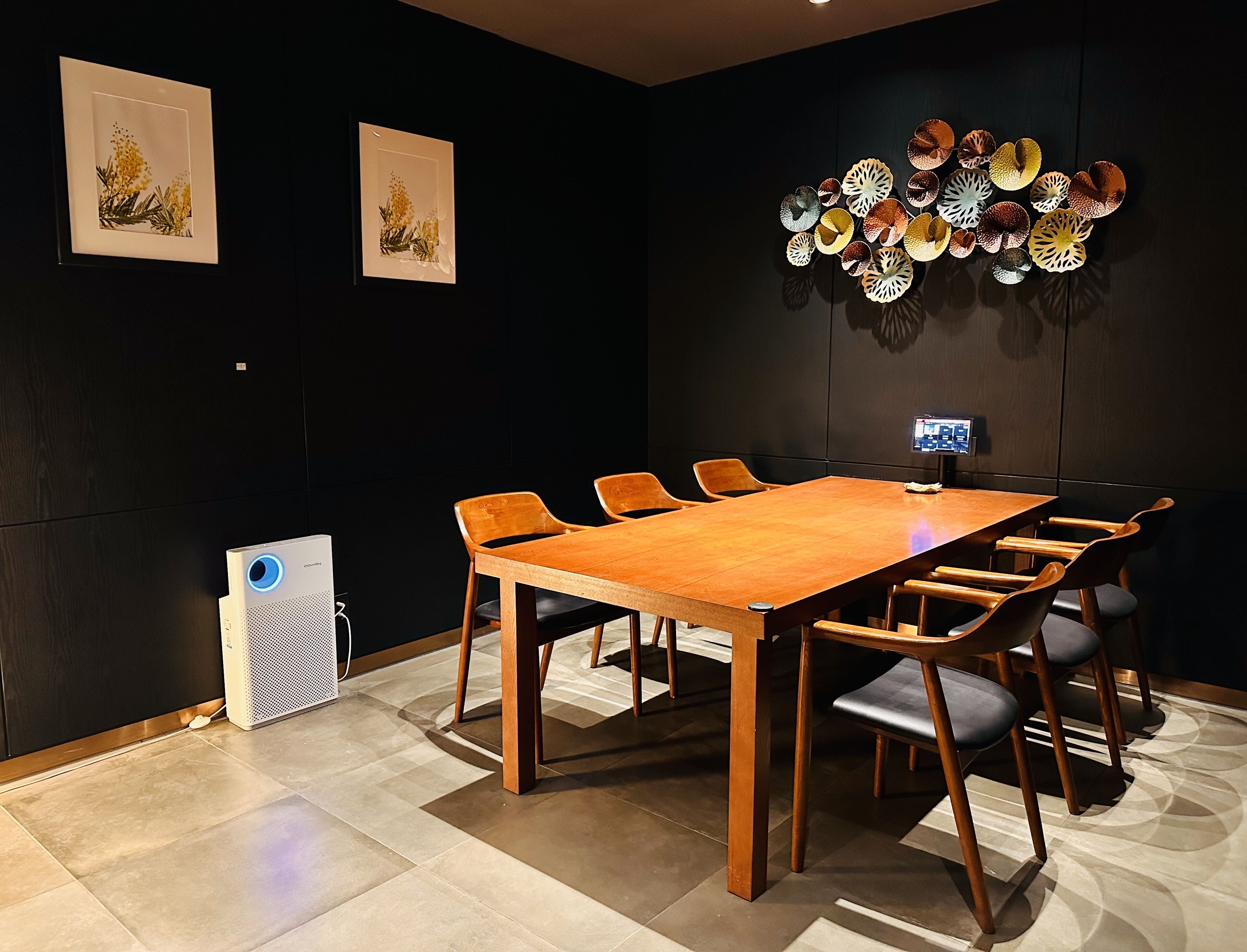 A conference room with a long wooden table, six chairs, and two framed botanical prints on the wall.