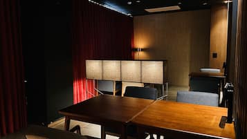 Un salón de conferencias con una mesa de madera, sillas, una lámpara grande y una cortina roja.
