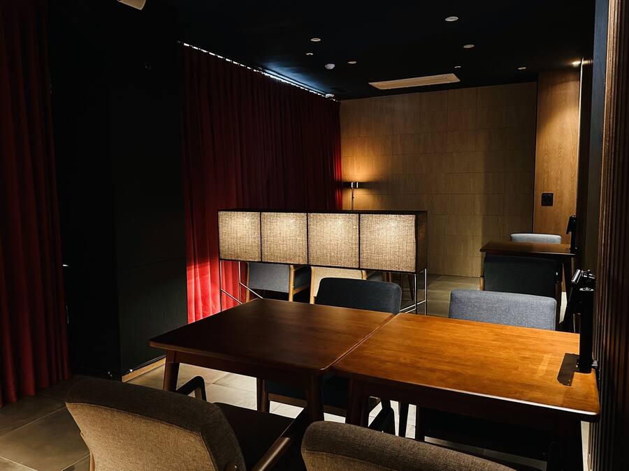 Un salón de conferencias con una mesa de madera, sillas, una lámpara grande y una cortina roja.