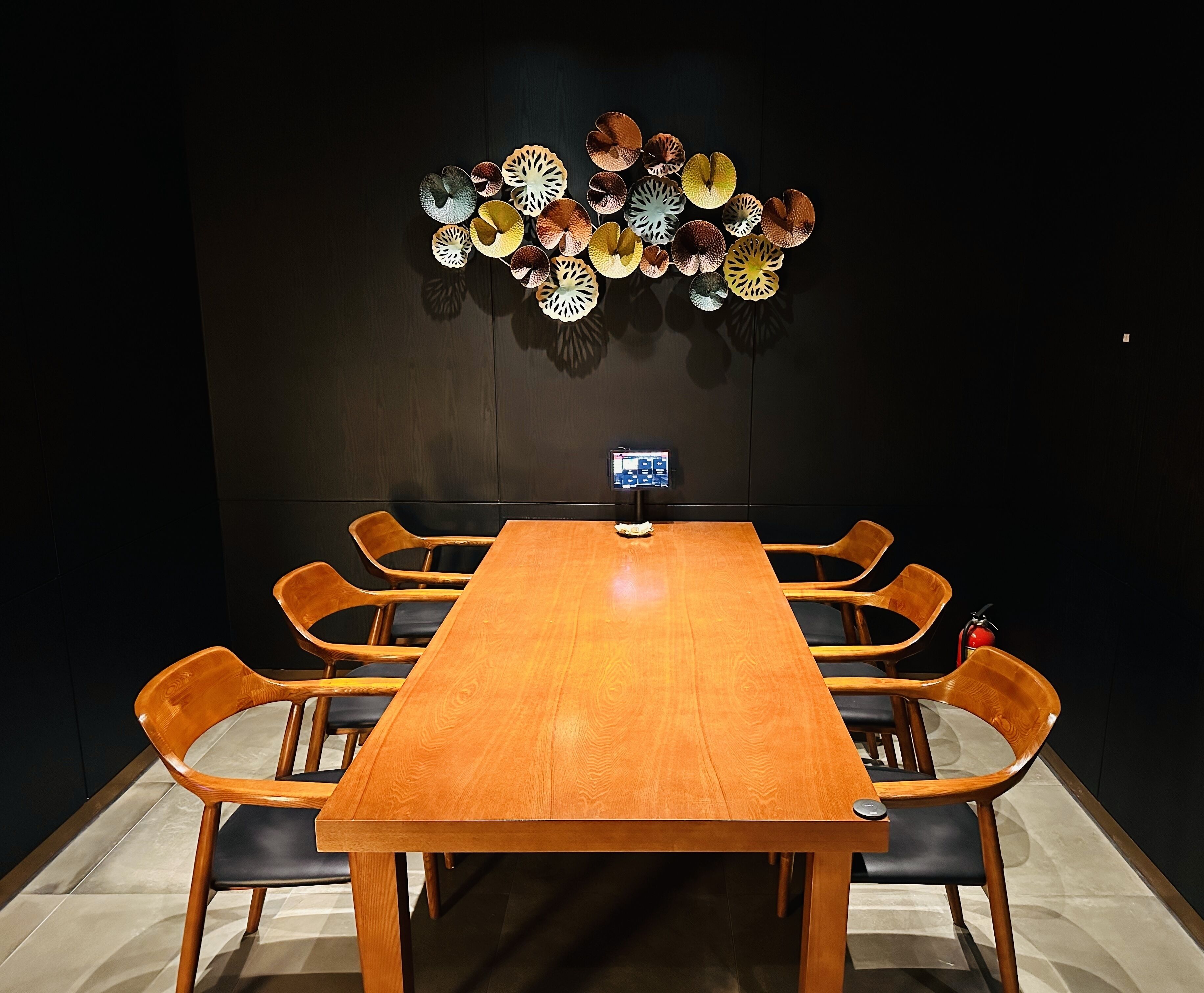 A conference room with a long wooden table, six wooden chairs, and a decorative wall piece above the table.