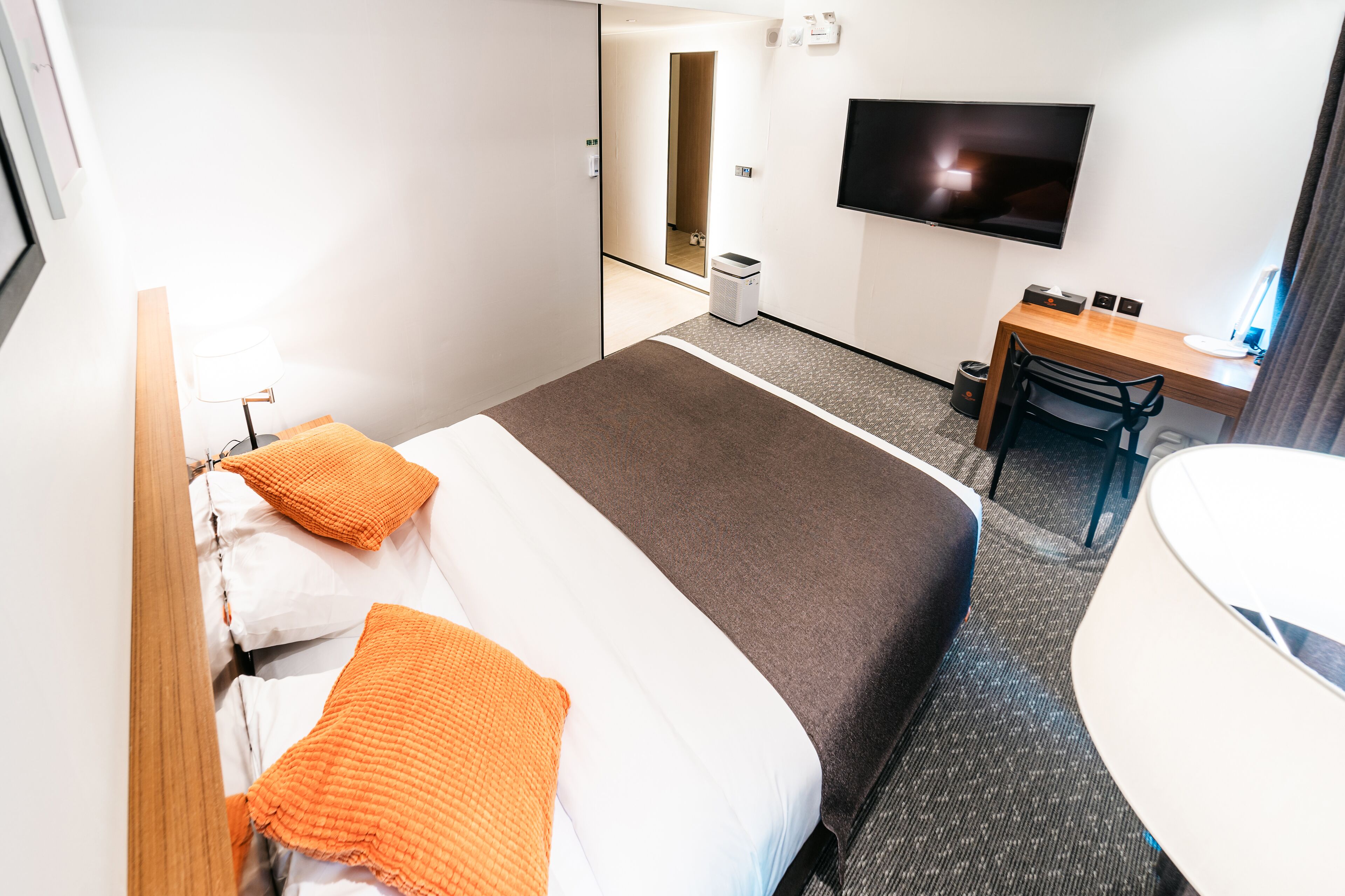 Ett hotellrum med en säng, ett skrivbord, en stol, en tv och ett badrum.