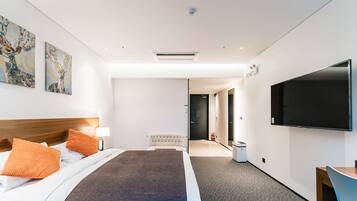 A modern hotel room with a large bed, two orange pillows, a flat-screen TV, and artwork on the walls.