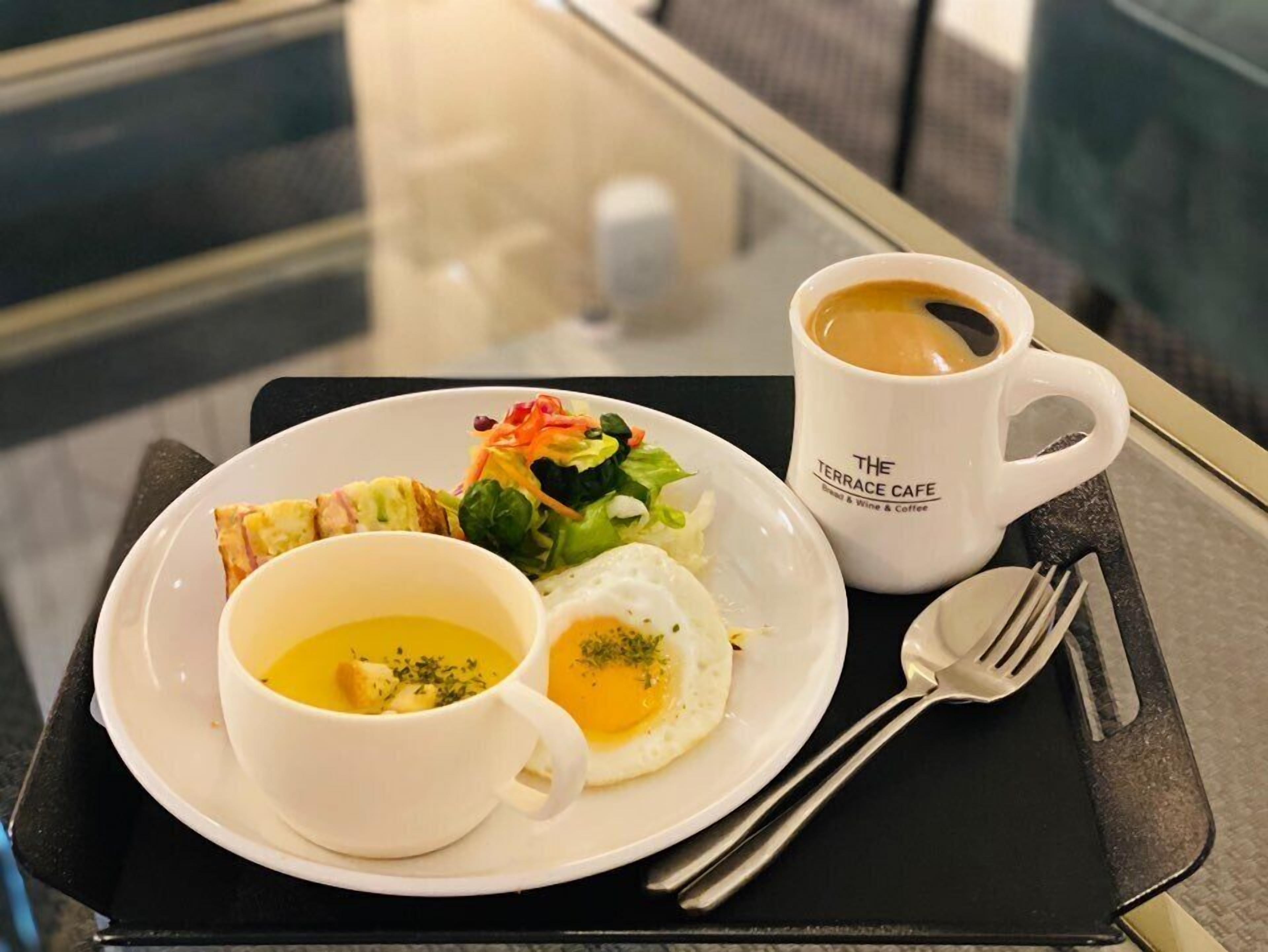 A tray with a plate of food including a salad, two eggs, and soup, accompanied by a cup of coffee and cutlery.