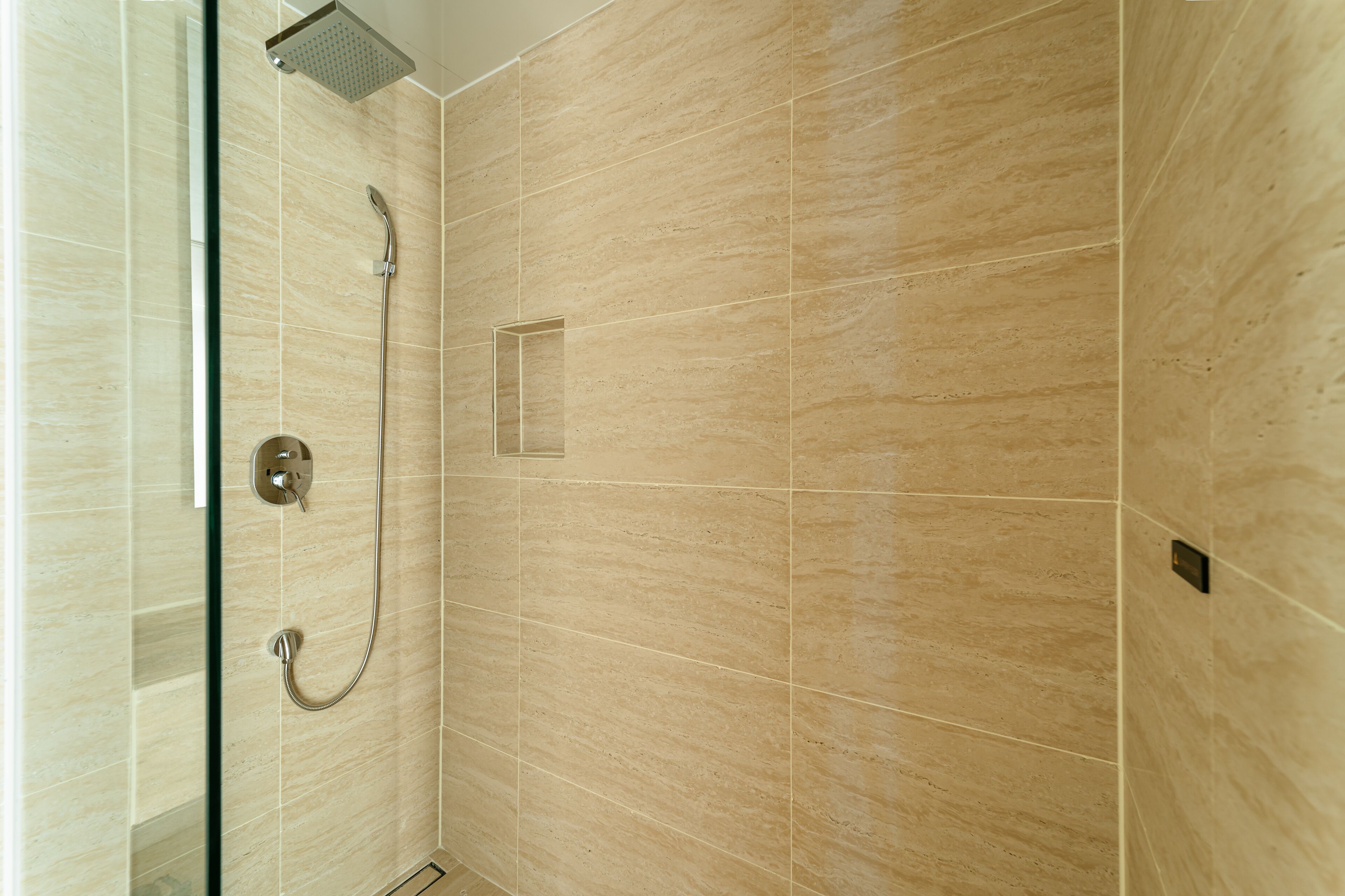 A modern bathroom with beige tiles, a glass shower enclosure, and a handheld showerhead.
