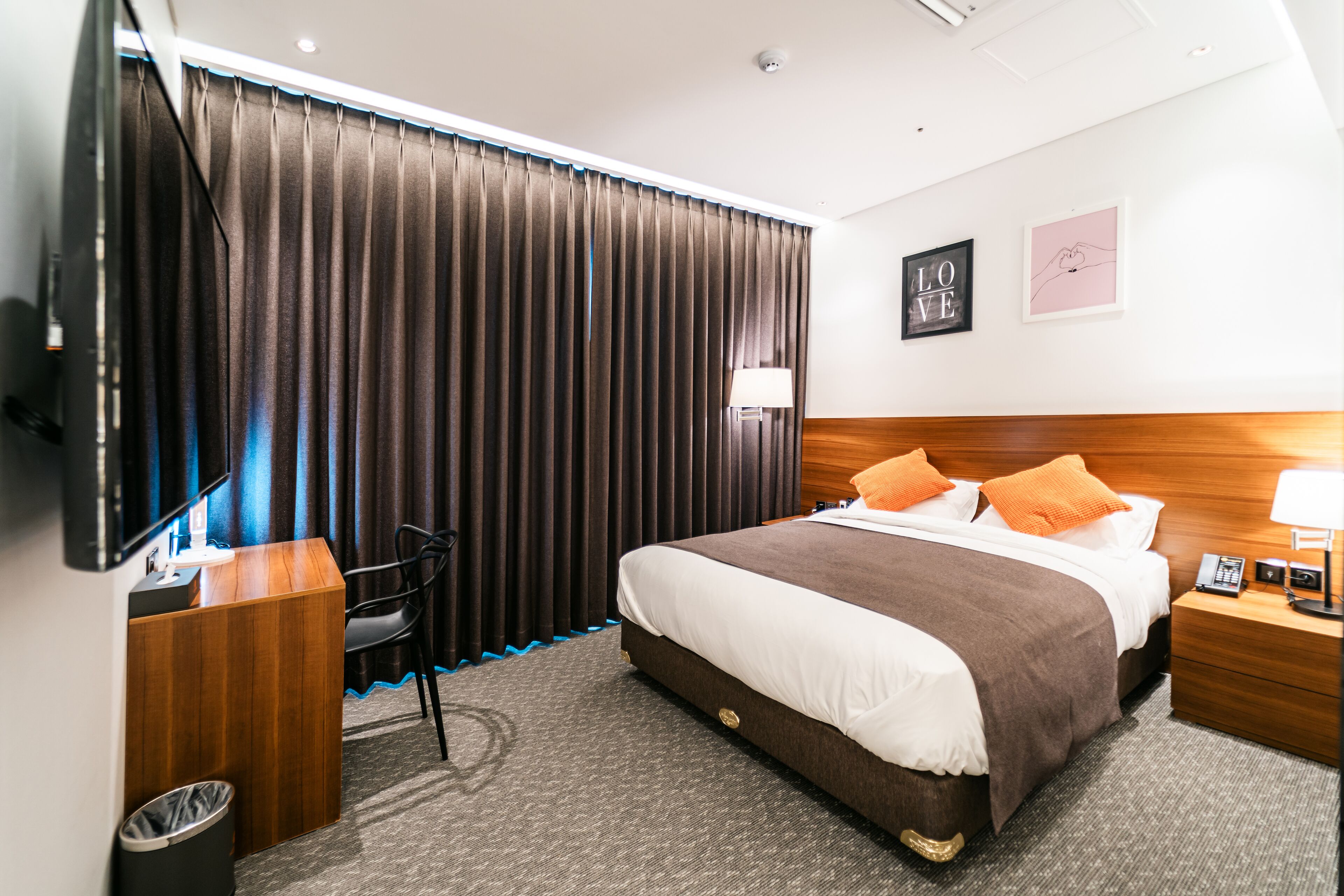 Een hotelkamer met een bed, nachtkastje, lamp en een tv op een standaard.