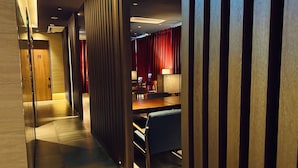 A modern hotel lobby with a wooden reception desk, a seating area with a table and chairs, and a red curtain backdrop. - Hotels One (Wanju)