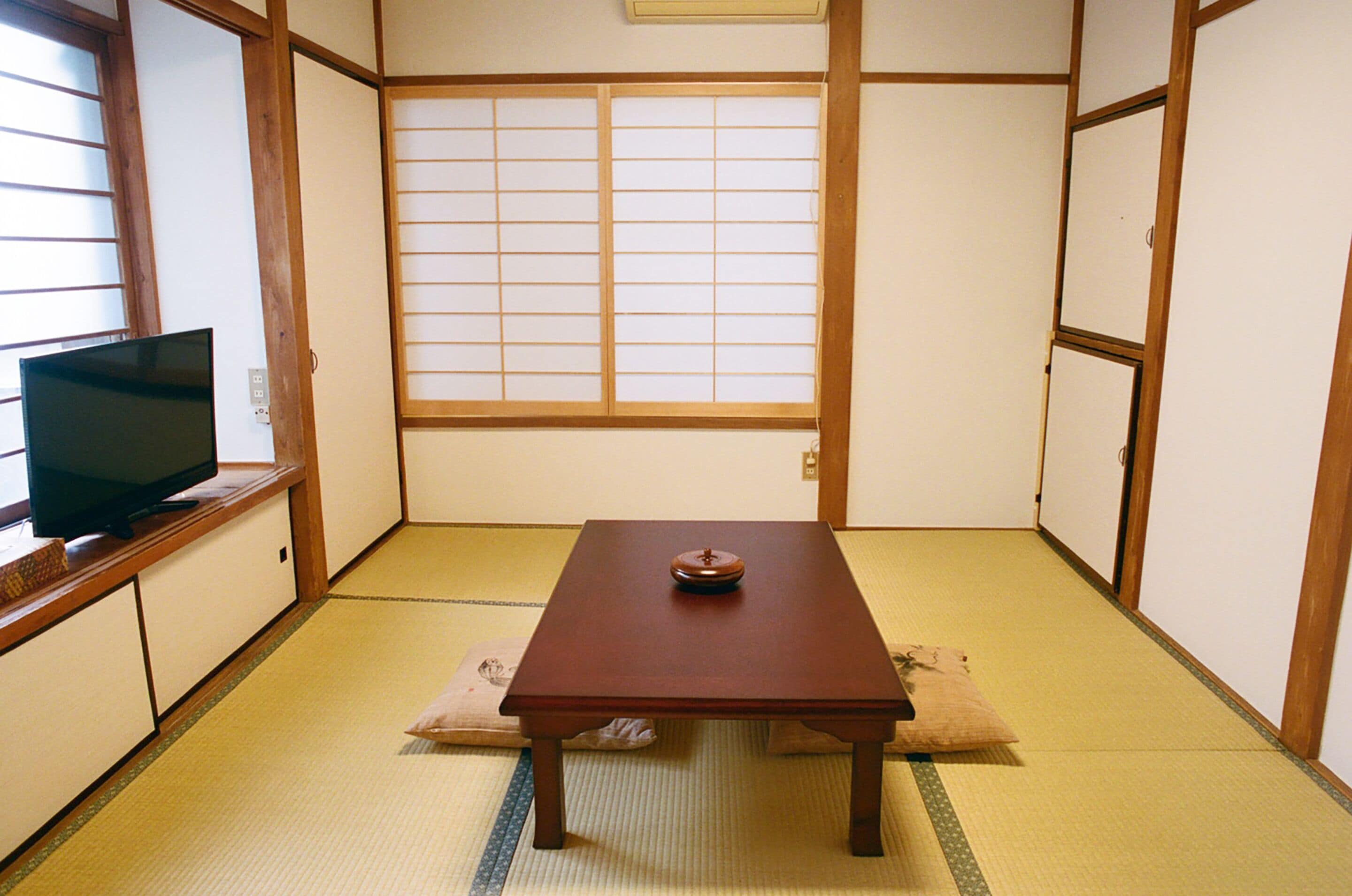 A traditional Japanese room with tatami flooring, a low wooden table with a decorative item, and a television on a low cabinet.