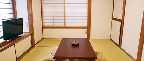 A traditional Japanese room with tatami flooring, a low wooden table with a decorative item, and a television on a low cabinet.