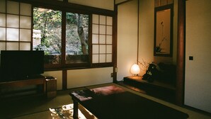 A traditional Japanese room with tatami flooring, a television, a lamp, and a view of greenery outside. - Hakonowa Hot spring inn (Hakone)