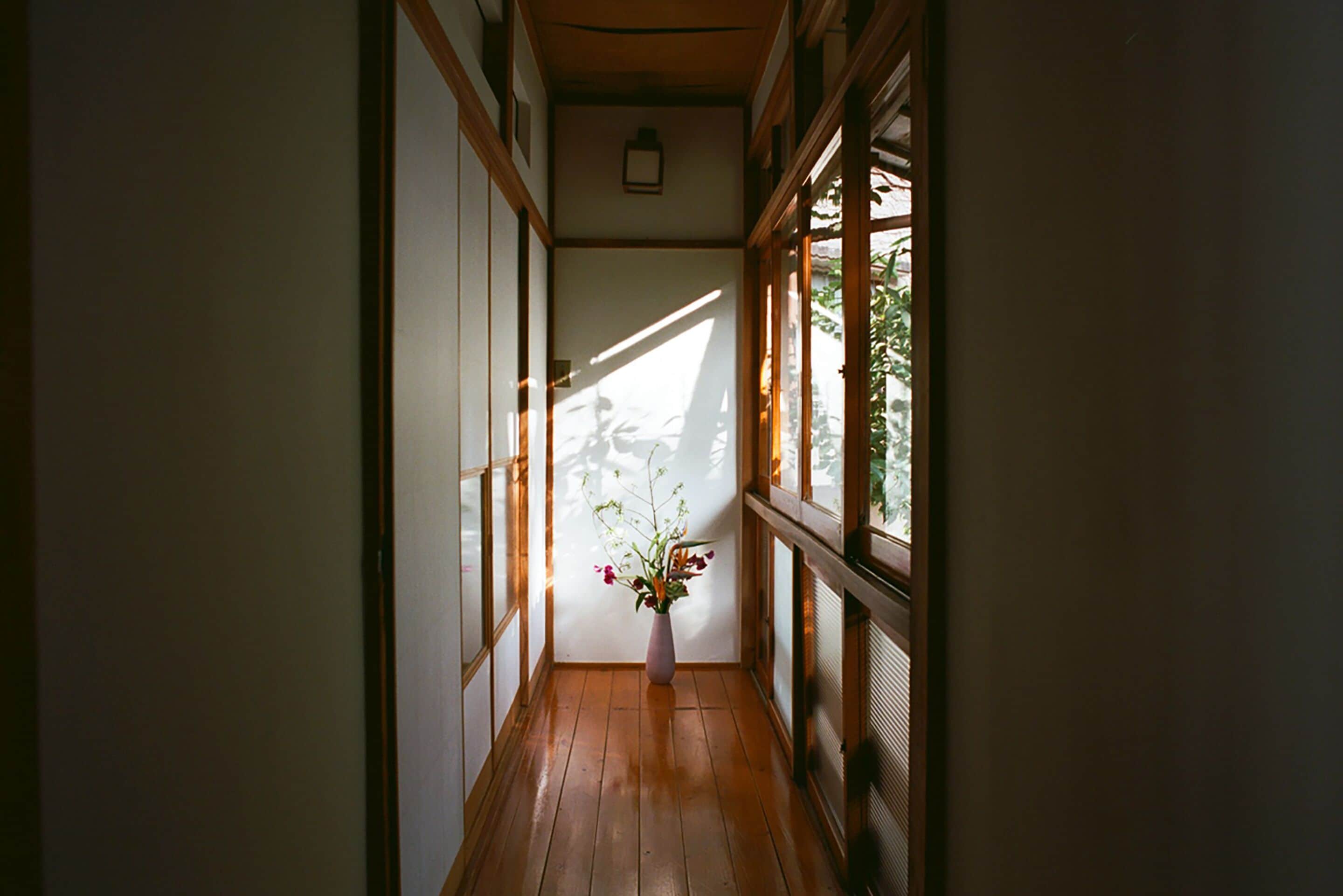 A narrow corridor with wooden flooring and large windows on one side.