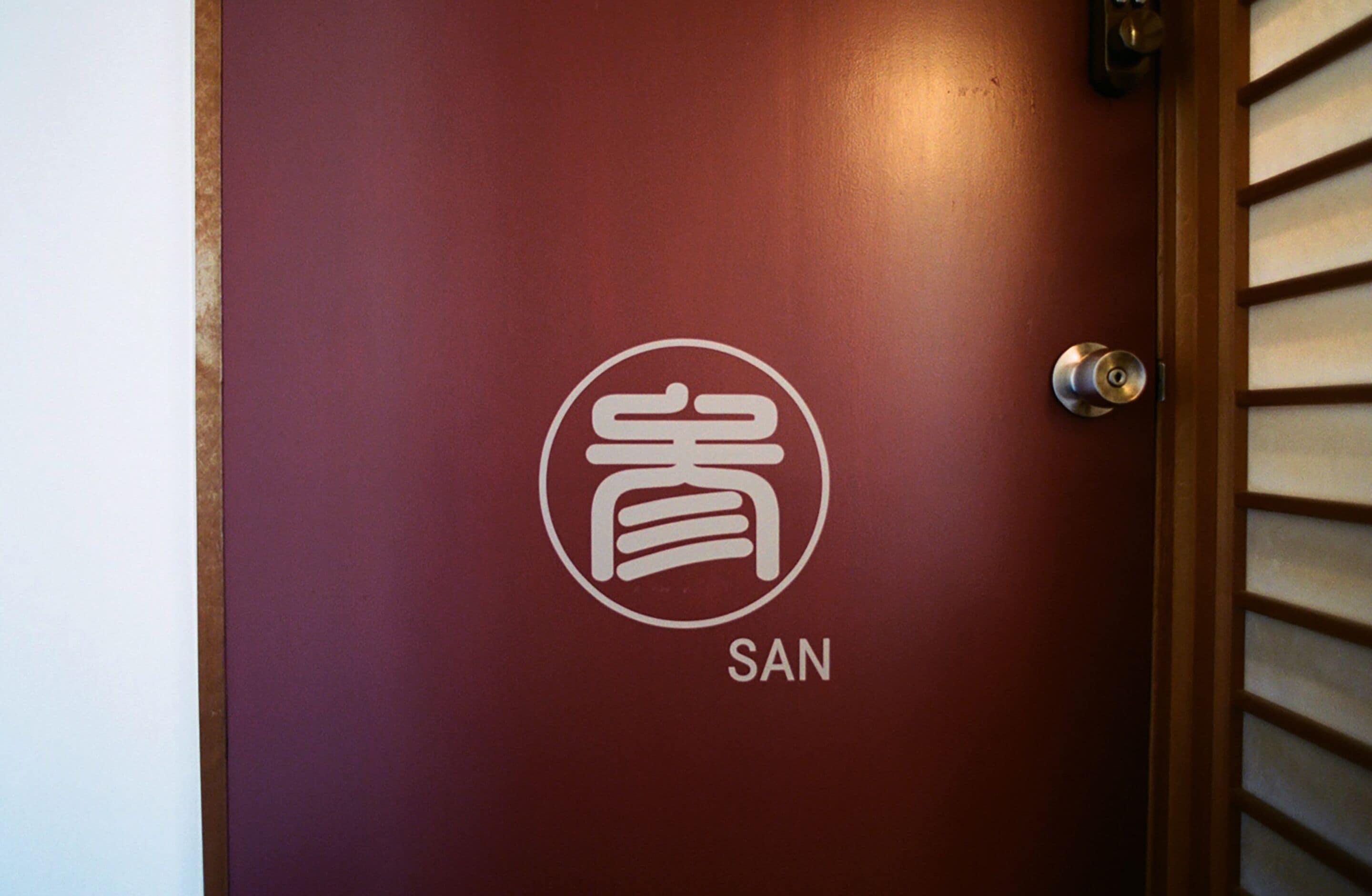 A maroon door with a white logo and the word "SAN" below it.