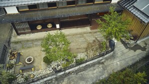 Uma casa japonesa tradicional com telhado de telhas, varanda de madeira e um pequeno jardim com pedras e plantas.