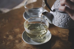 A clear glass teapot pouring water into a glass cup on a saucer.