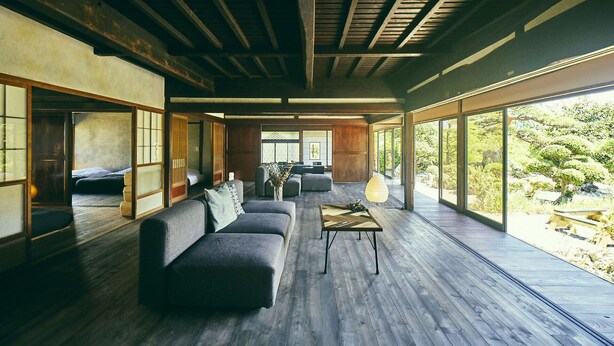 Une pièce spacieuse dotée d’un plancher en bois, d’un canapé, d’une table et de grandes fenêtres donnant sur un paysage verdoyant.