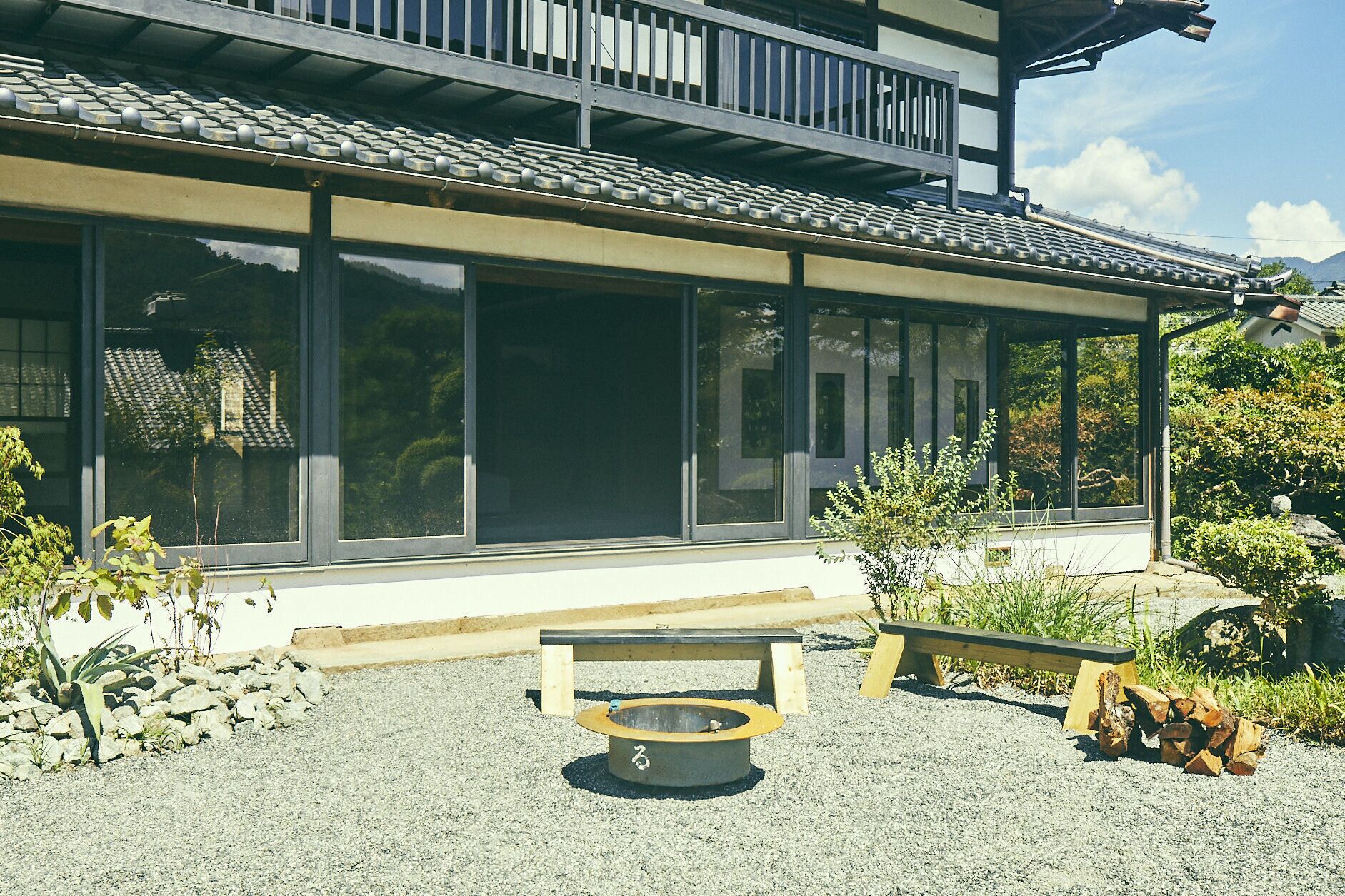 Un edificio tradicional con amplias ventanas, un patio cubierto y una pequeña zona de estar exterior con banco y una chimenea.
