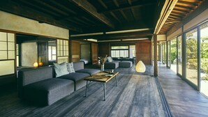 Un vaste espace de vie comprenant un canapé, une table basse et des objets décoratifs. De grandes fenêtres laissent entrer la lumière naturelle et offrent une vue sur l’extérieur.