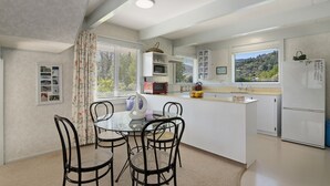 A modern kitchen with a dining area, white cabinetry, a refrigerator, and a window with a scenic view. - Pukenui Paradise - Havelock Holiday Home (Havelock)