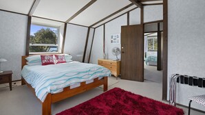A bedroom with a bed, a dresser, a red rug, a fan, and a view of the outdoors. - Pukenui Paradise - Havelock Holiday Home (Havelock)