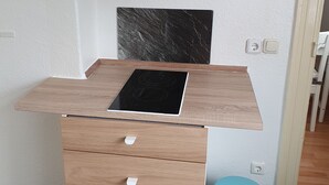 Una kitchenette con encimera de madera, estufa empotrada, un mueble superior y un cubo de basura.