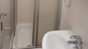 Un baño con ducha envuelta en vidrio, un lavamanos blanco y un espejo sobre él.
