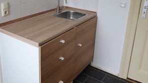 Cocina compacta con encimera de madera, pileta de acero inoxidable y salpicadero de azulejos blancos.