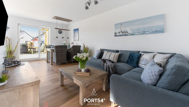 Un salon moderne avec un canapé gris, une table basse en bois et une vue sur l’extérieur grâce à une porte vitrée.